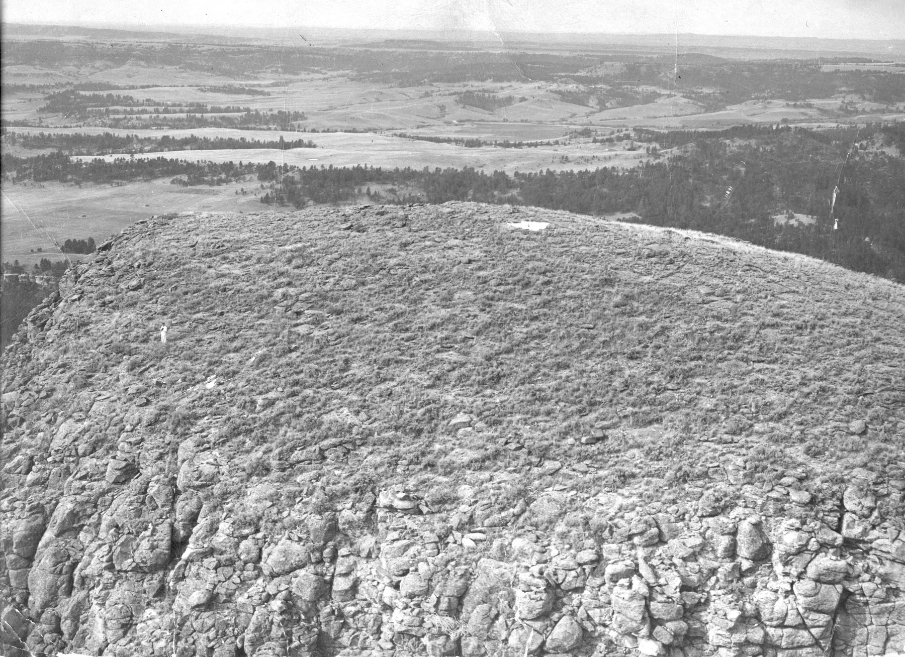 George Hopkins standing on the rocky summit of Devils Tower with the distant landscape below