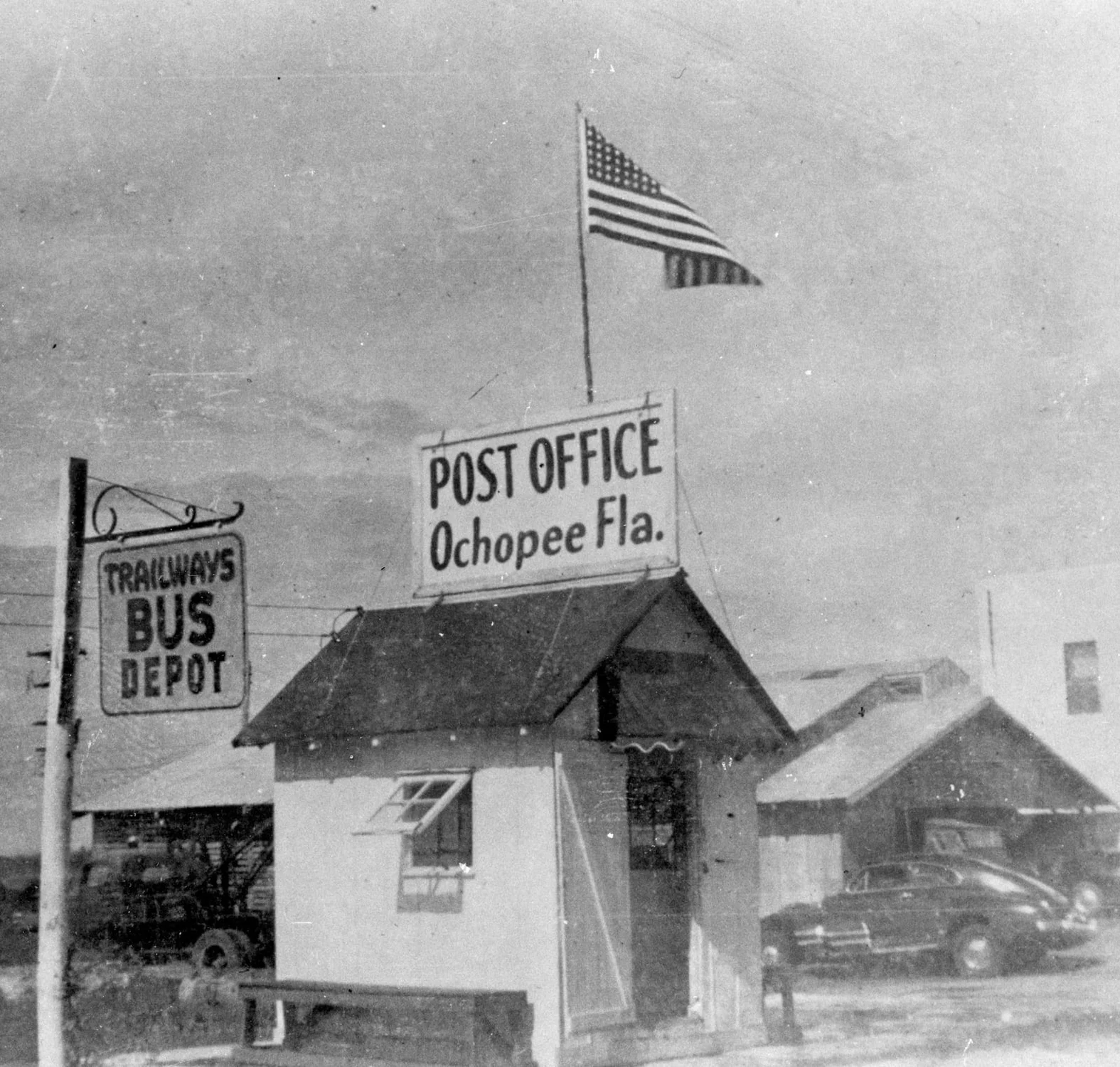 Tiny white Ochopee post office with a large sign and a flag above it