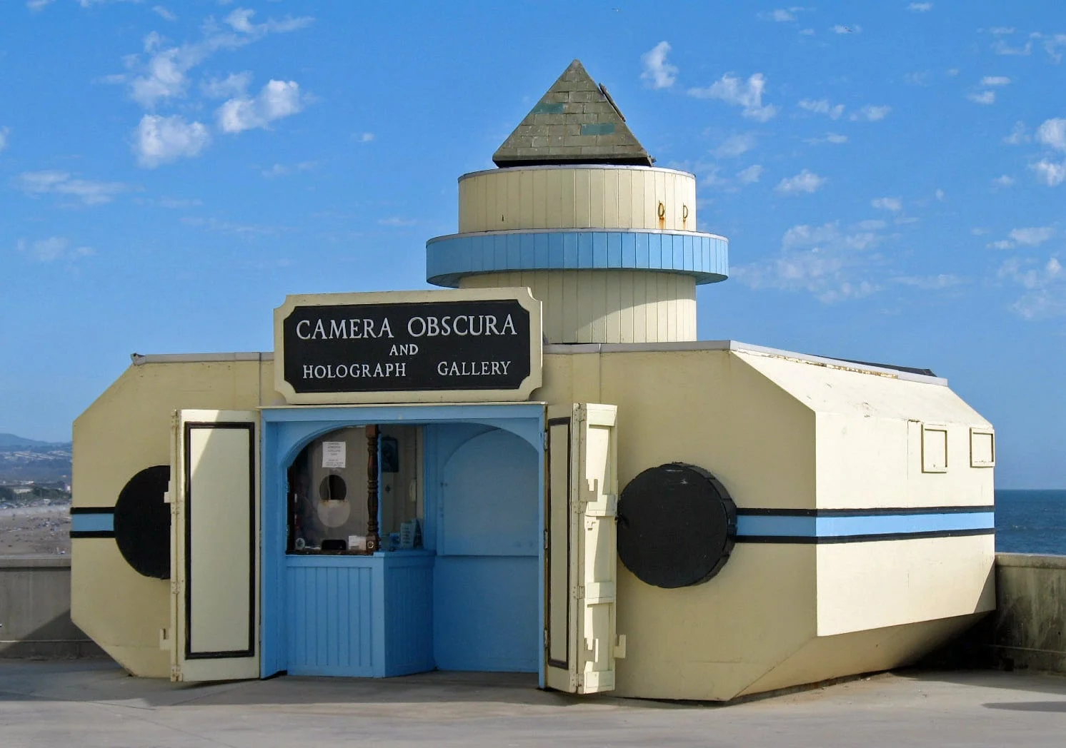 Small yellow camera-shaped building marked Camera Obscura beside San Francisco’s Cliff House