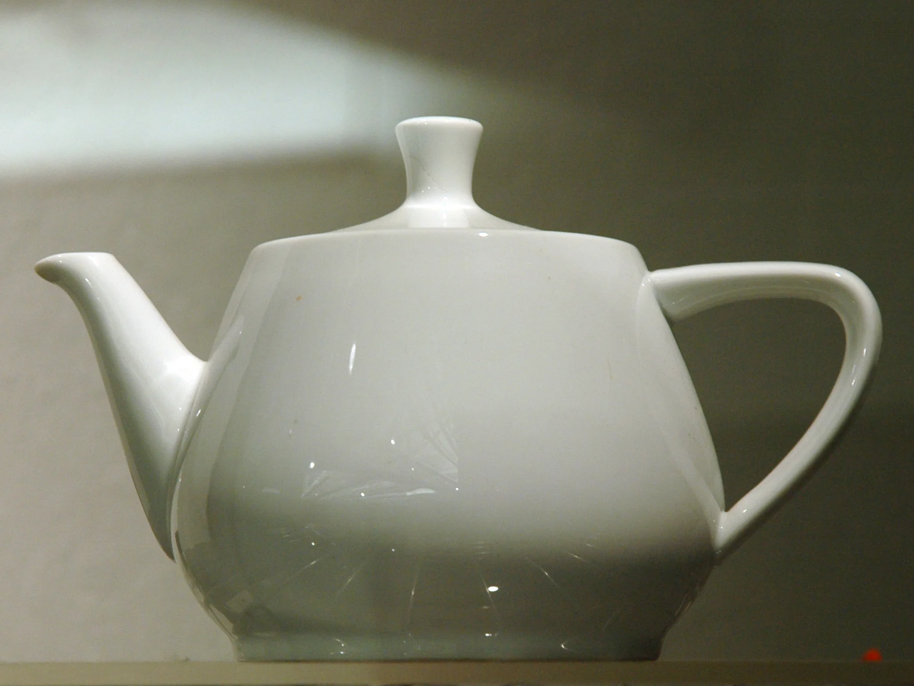 White ceramic teapot with a curved handle, projecting spout, and fitted lid